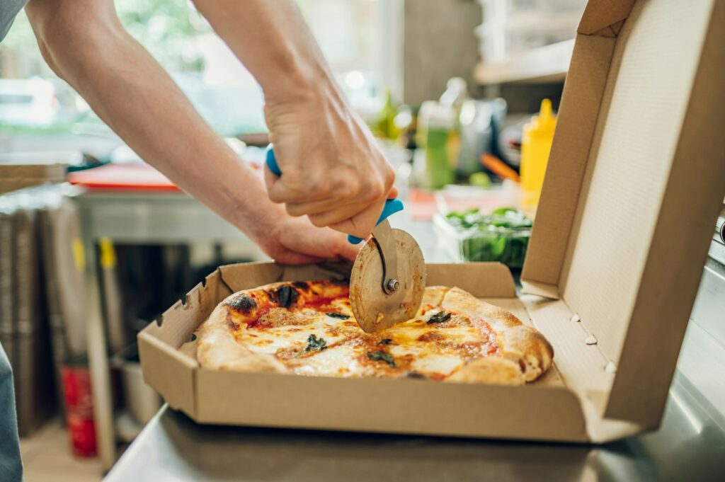 Hand of kitchen chef cutting pizza with a pizza cutter